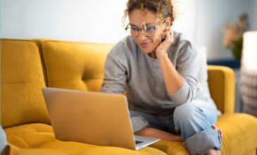 Woman on couch typing on laptop.